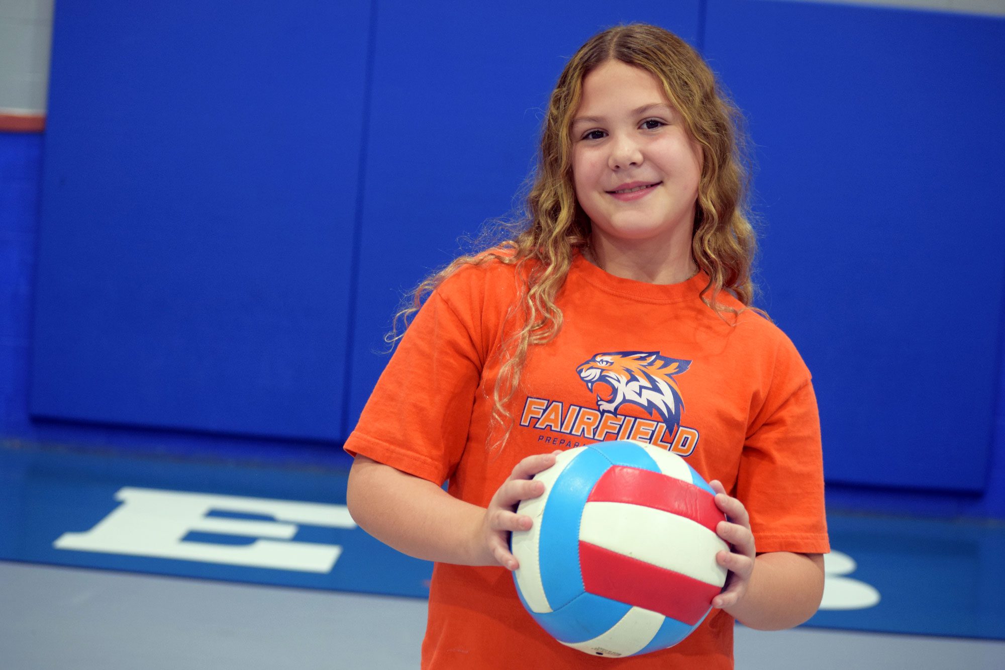 Smiling student holding a volleyball in front of a Fairfield Prep wall.