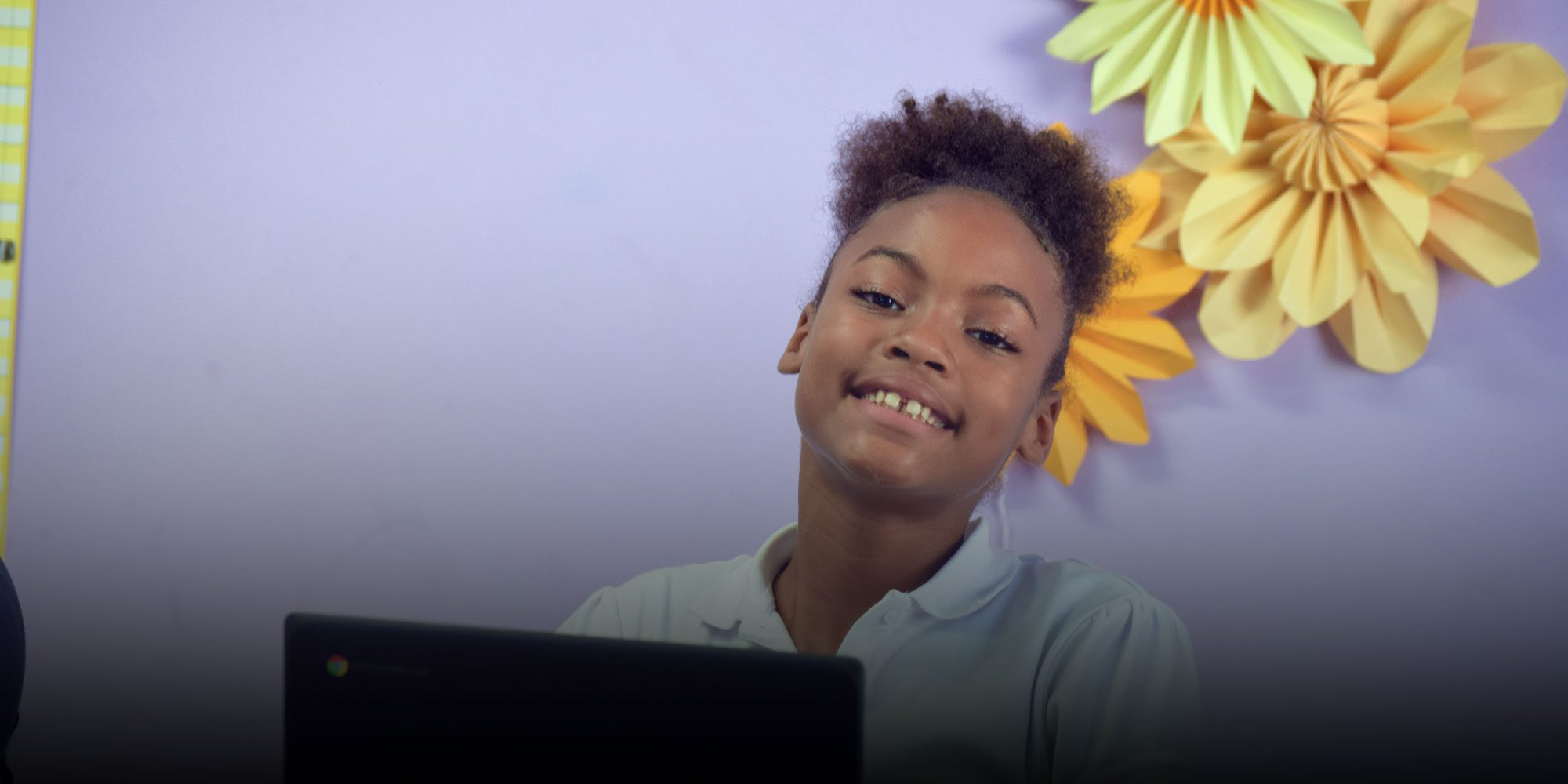Smiling student with curly hair sitting at a laptop.