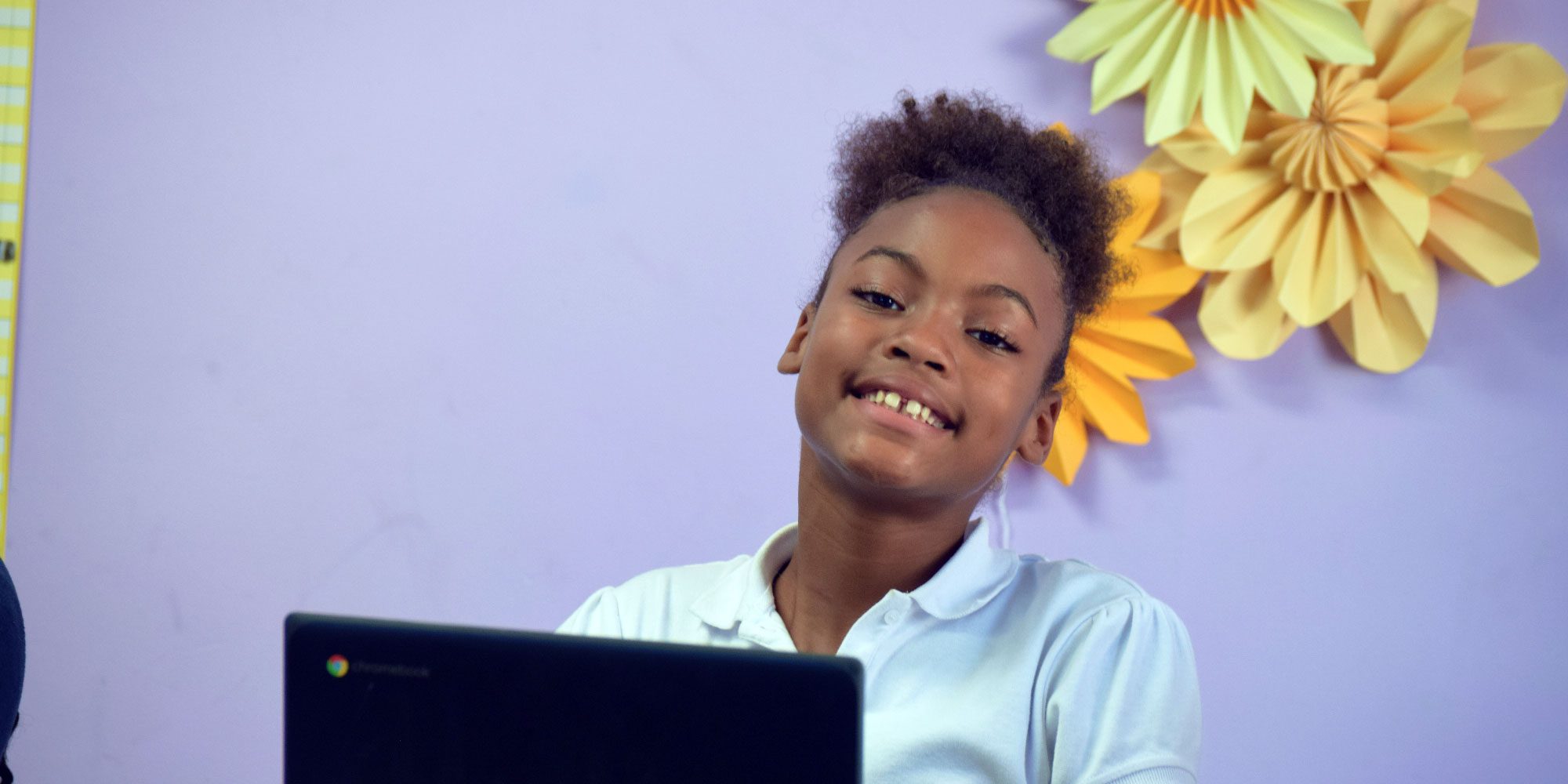 Smiling student with curly hair sitting at a Chromebook.